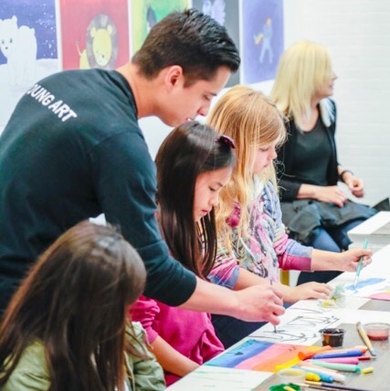 art teacher with paint brush teaching students during studio lesson