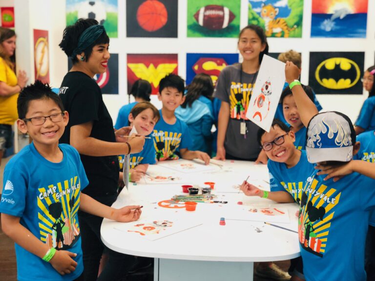 group of school children at art studio wearing blue shirts with paint supplies on table