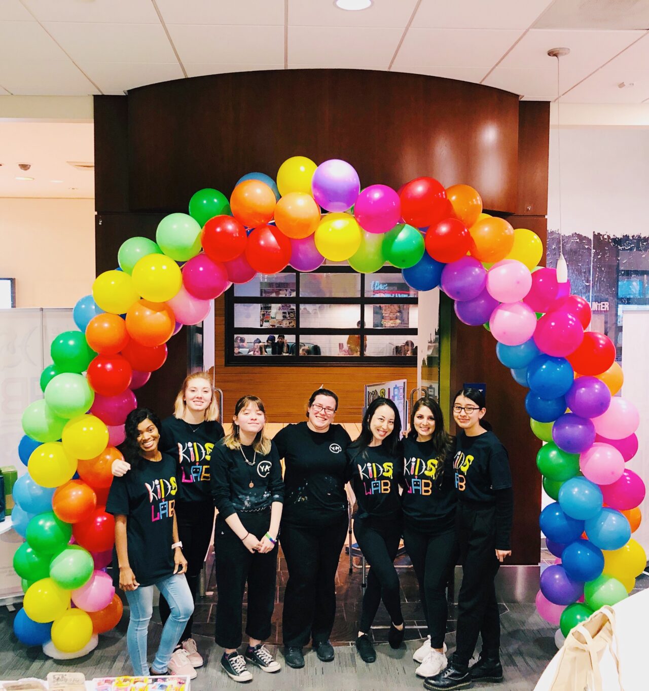 kids lab grand opening. team members standing under colorful balloon arch