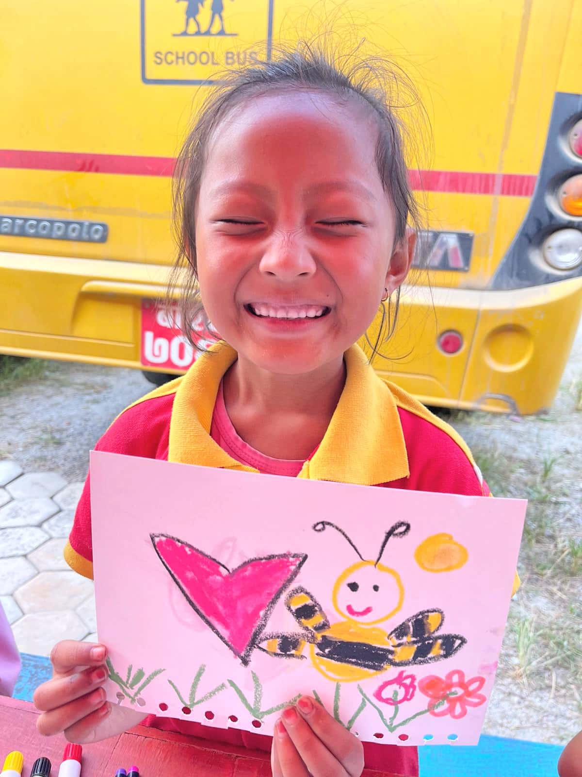 image of a girl holding her drawing of a heart and bee and smiling