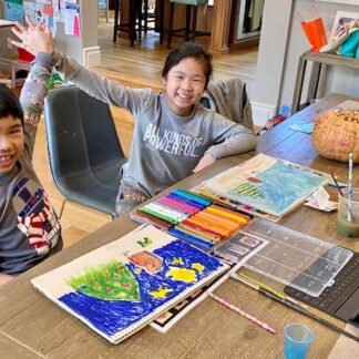 2 students smiling and giving each other a high five. art supplies on table in front of them