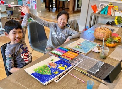 2 students smiling and giving each other a high five. art supplies on table in front of them