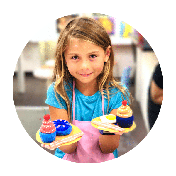 girl holding clay sculpture of cupcakes