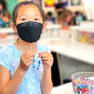 student making a bracelet with a bucket of beads