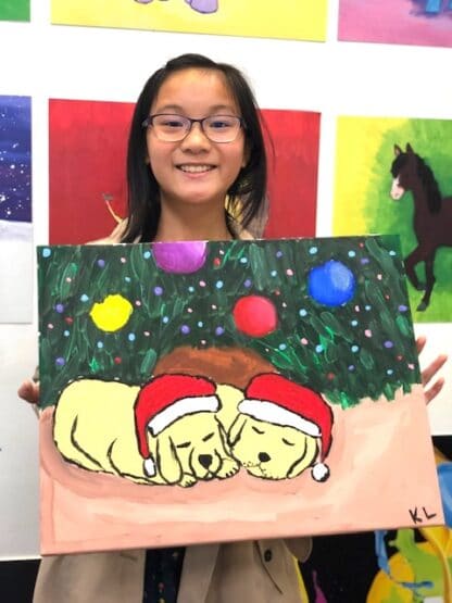 image of student holding painting with two puppies under a decorated evergreen