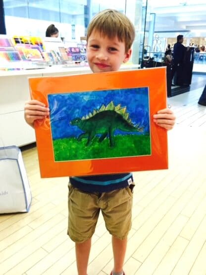 image of student holding dinosaur painting with orange border