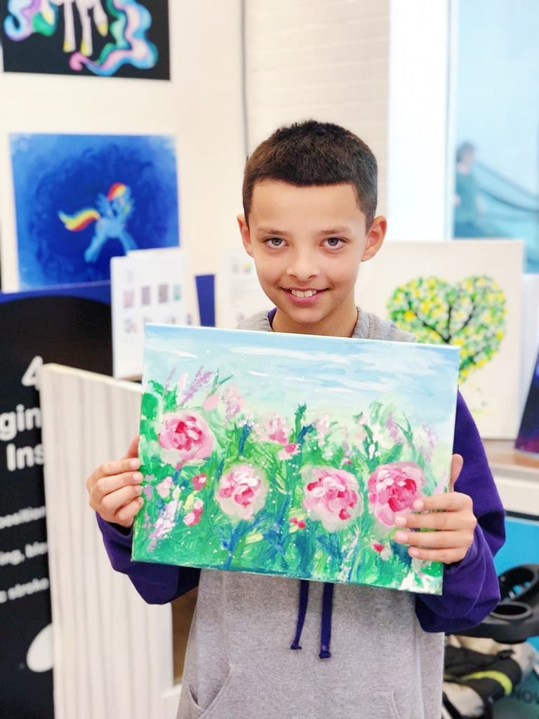 boy holding canvas painting of pink flowers with green and blue background