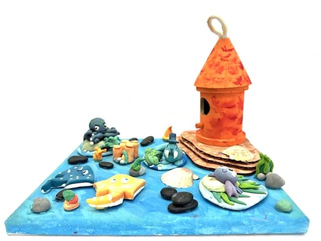 image of a blue canvas with an orange birdhouse in the corner. several small clay items surround the birdhouse