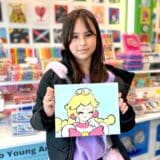 image of a young girl holding up her painting of an anime style character in pink