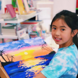 image of a young girl holding a painting of a sunset on a canvas