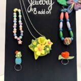 image of an easel with a canvas holding several different types of handmade jewelry such as bracelets, rings, and necklaces in full color