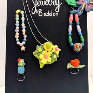 image of an easel with a canvas holding several different types of handmade jewelry such as bracelets, rings, and necklaces in full color