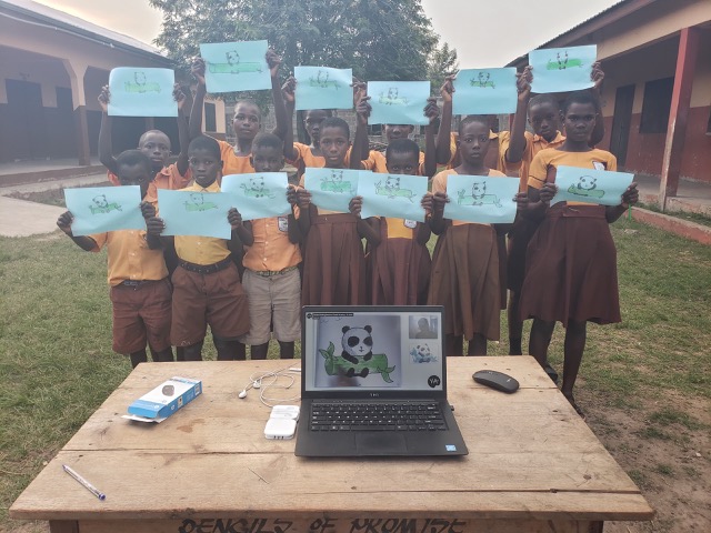 image of a group of school girls in ghana holding up their art with a laptop on a table in front of them